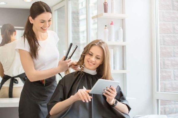 A stylist curling a smiling client's hair in a bright salon